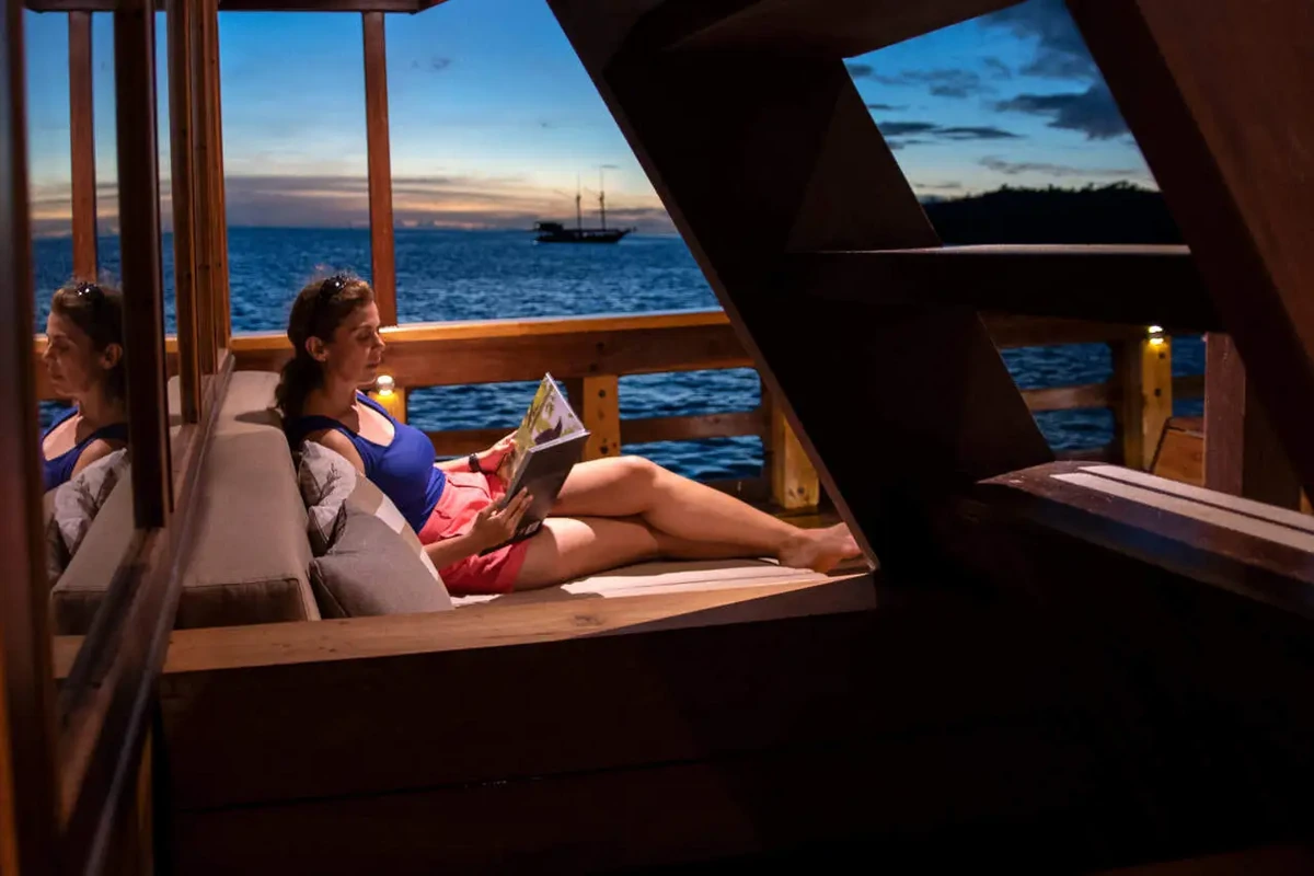 Guests reading on a shaded liveaboard lounge deck looking out to sea