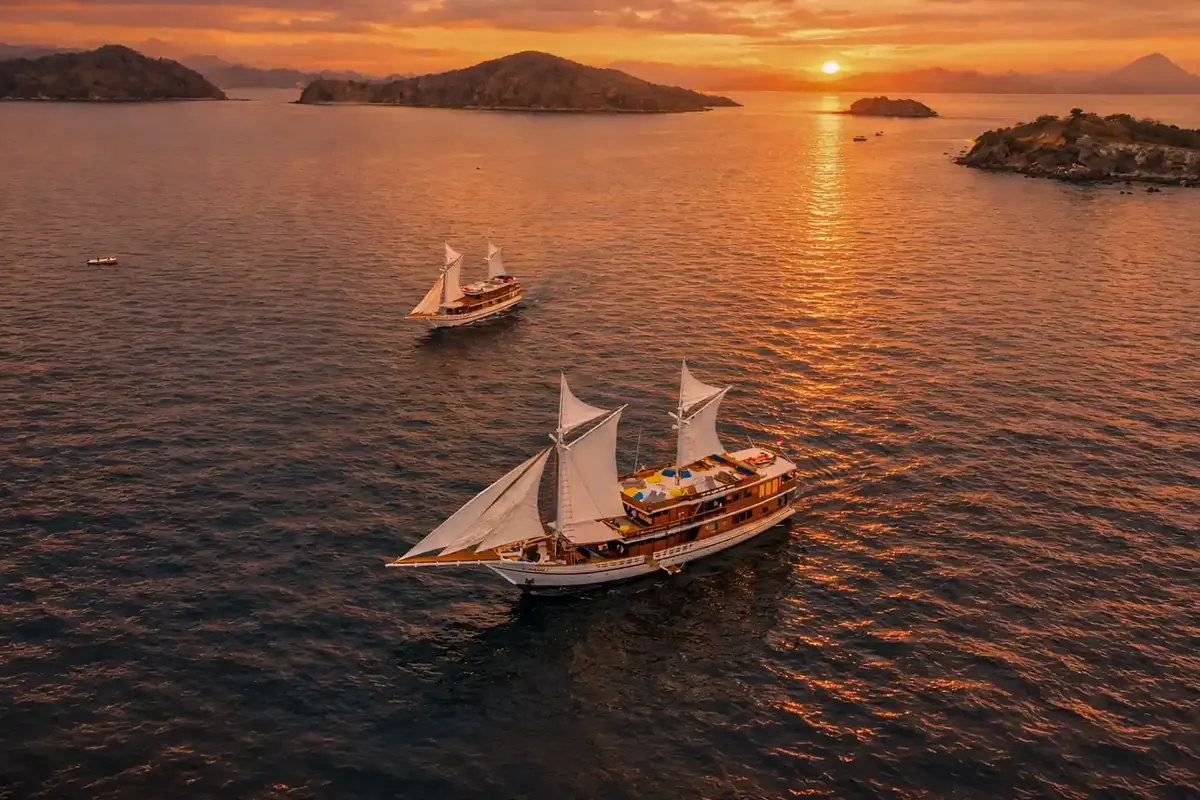 A phinisi under sail on a glassy sea at sunset seen from above