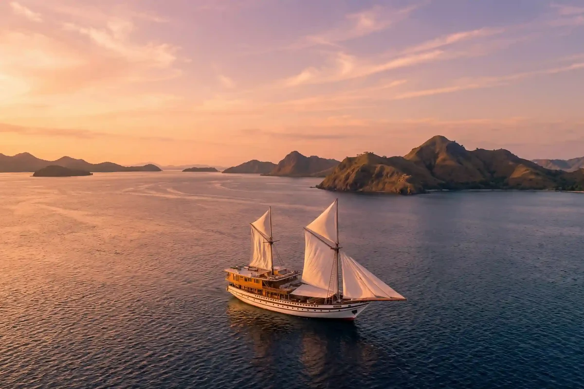 A phinisi anchored in a quiet bay under a pink evening sky